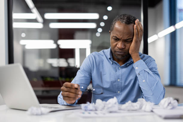 istock Stressed office worker dealing with frustration at desk surrounded by crumpled papers. Overwhelmed businessman holding glasses next to laptop, experiencing workplace stress and fatigue. 2174700733