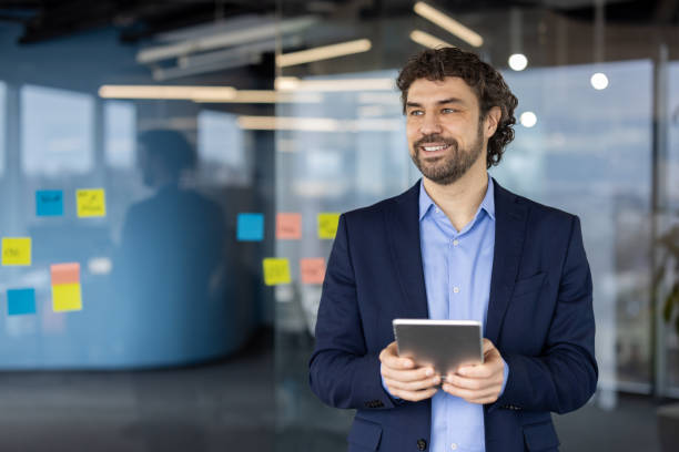 istock Confident businessman using digital tablet in modern office with glass walls and sticky notes 2174711022