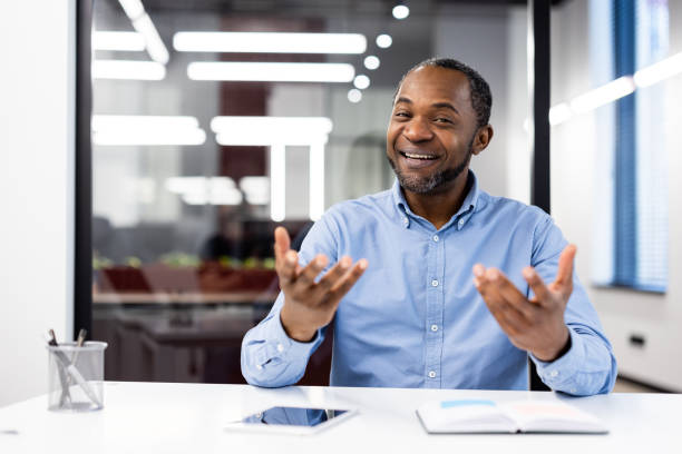 istock Confident smiling businessman giving presentation during a meeting in modern office setting with smartphone and open notebook on desk 2174712456