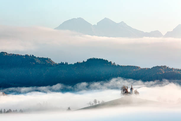 The morning mist gently covers the chapel on the hillside, with distant mountains faintly visible, adding a sense of mystery and tranquility. The entire scene feels dreamlike, as if time stands still in this serene moment.