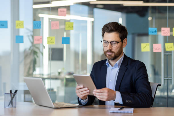 istock Focused businessman in suit working on tablet at modern office with colorful post-it notes and laptop 2174718407
