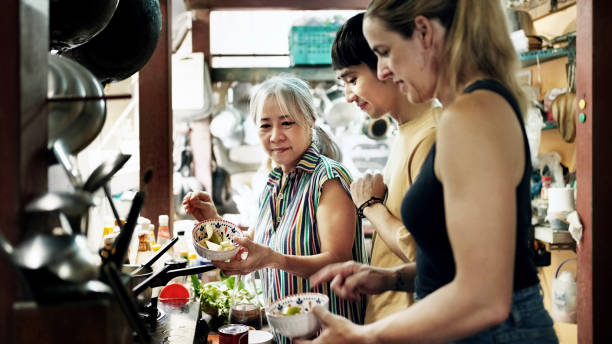 Senior woman teaching thai cooking to tourists in kitchen stock photo