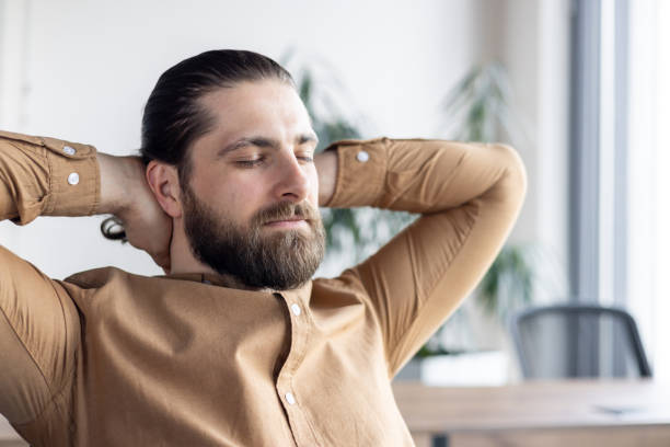 istock Relaxed businessman with beard leaning back in office chair taking a break in modern workplace with sunlight streaming through window 2174719527