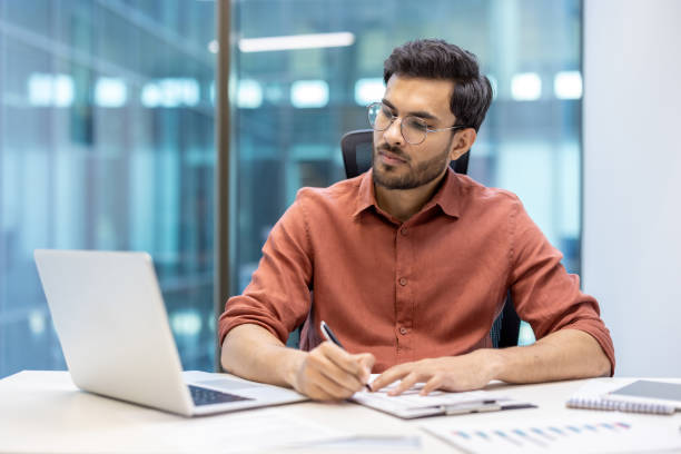 istock Serious financier working at desk in modern office, using laptop and taking notes with focus and concentration. 2174722400