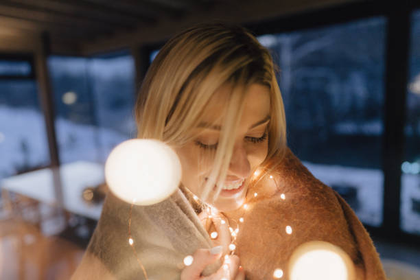 Photo of a young woman holding string lights during Christmas decoration of her house