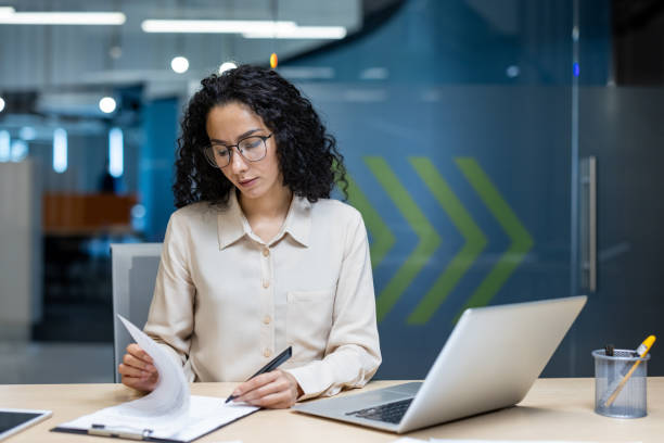 istock Hispanic businesswoman in modern office setting serious and focused while analyzing documents at desk 2174723916