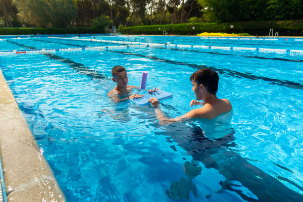 istock Swimming instructor helping blind teenager student with floating board in pool 2174724895