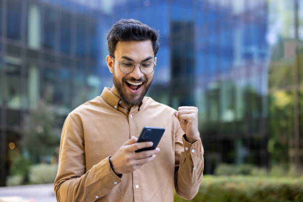 istock Excited young man celebrating success while checking message on smartphone outdoors in urban setting 2174726382