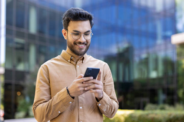 istock Smiling young man using smartphone outdoors against modern office building, portraying connectivity and technology in urban environment 2174727907