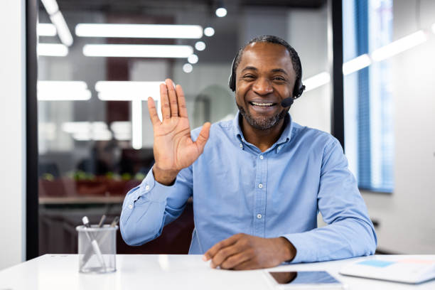 istock Smiling businessman in modern office waving during a video call with headset for a professional meeting 2174729805