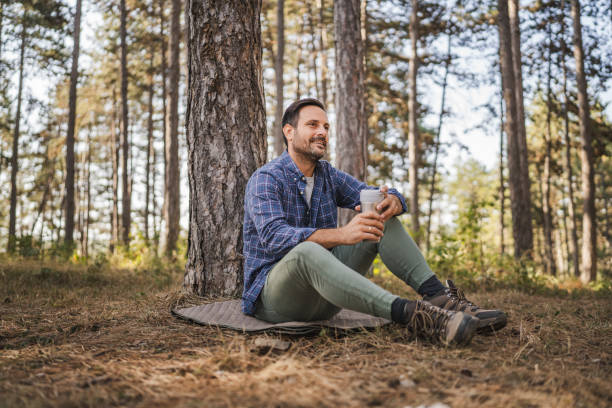 istock Adult man sit on mat in front tree and drink coffee from thermos 2174731829