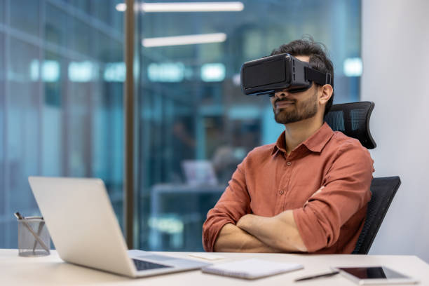 istock Young professional wearing virtual reality headset sitting at office desk using innovative technology for immersive experience 2174732192