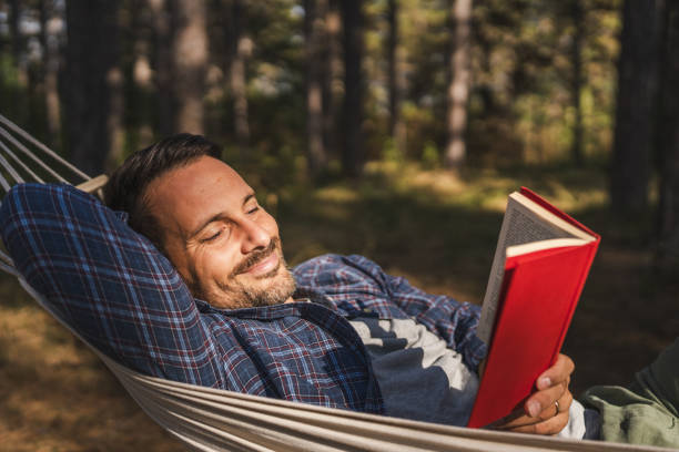 istock Adult man lying down and read book in hammock 2174732383