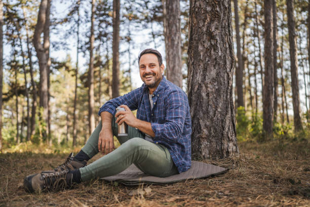 istock Adult man sit on mat in front tree and drink coffee from thermos 2174732500
