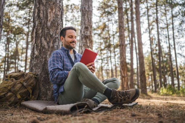 istock Adult man sit on mat in front tree and read book 2174732596