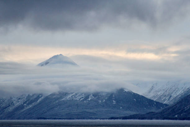A peak in the Chugach Mountain range shrouded in clouds in fading winter light.