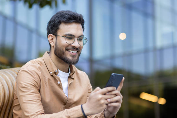 istock Smiling man using smartphone outdoors with modern glass building in background enjoying communication 2174736058