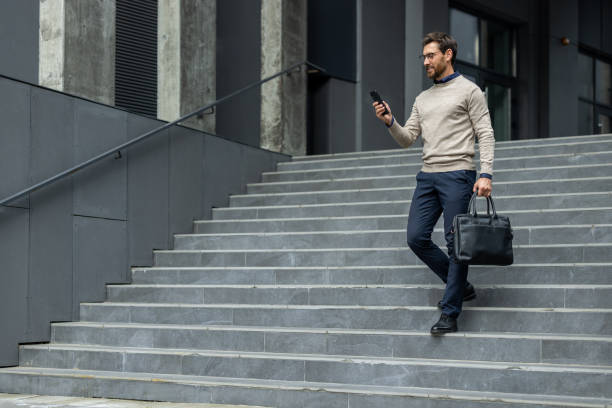 istock Confident businessman walking down steps while checking smartphone, dressed in smart casual attire, carrying black leather briefcase, conveying professional urban lifestyle 2174739792