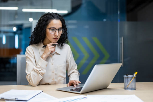 istock Focused businesswoman working on laptop in modern office environment, analyzing data and documents with serious expression 2174740578