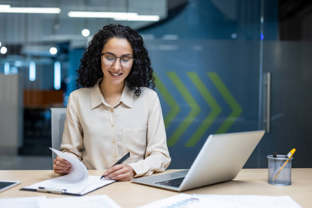 istock Hispanic businesswoman working at desk with laptop and documents in modern office setting 2174740950