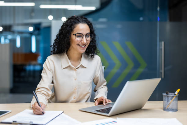 istock Confident businesswoman working on laptop in modern office, smiling and analyzing documents with focus and determination 2174741180