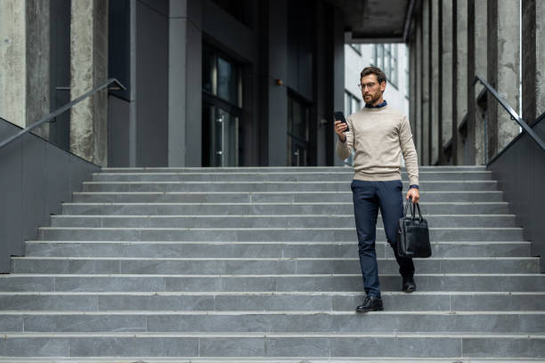 istock Confident businessman walking down stairs checking phone outside modern office building 2174741894