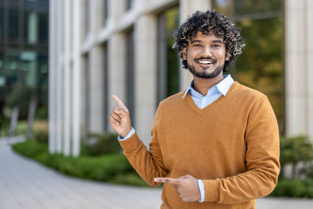istock Smiling young professional gestures confidently outside modern office building, embodying positivity and success 2174742727