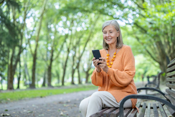 istock Smiling woman sitting on park bench using smartphone under lush green trees on a bright day 2174743047