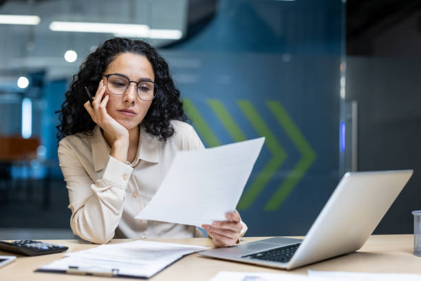 istock Hispanic businesswoman looking bored while analyzing documents at desk in modern office setting 2174743761