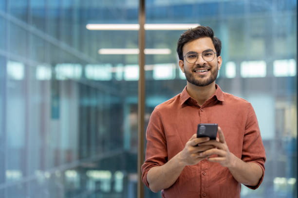 istock Confident young professional holding smartphone in modern office environment smiling at camera, showcasing successful business communication and positive attitude 2174743960
