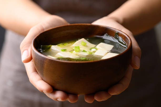 miso soup with tofu, wakame seaweed and spring onion in wooden bowl holding by hand, traditional japanese soup - misosoep fotos stockfoto's en -beelden