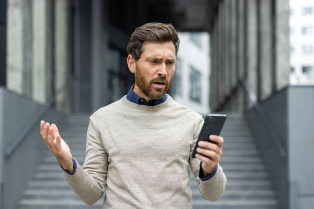 istock Frustrated businessman using smartphone outdoors, expressing confusion and stress in modern business environment 2174744774