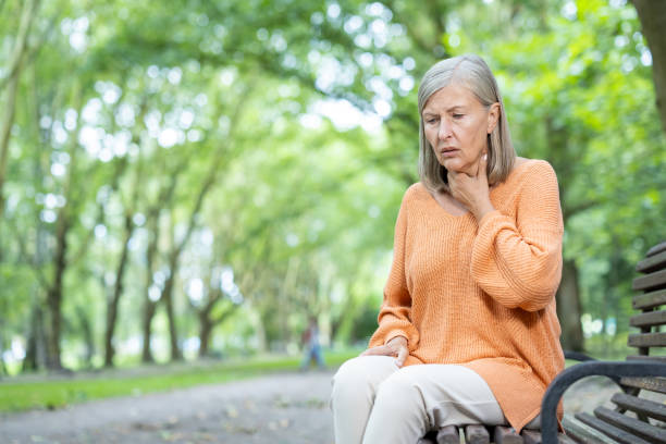istock Mature woman sitting on park bench outside looking concerned while touching her throat 2174747450