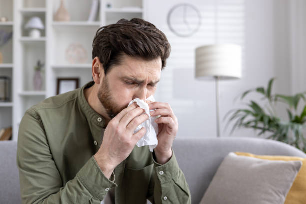 istock Young man sneezing into tissue in comfortable living room setting, experiencing seasonal allergies or common cold symptoms during daytime 2174749889