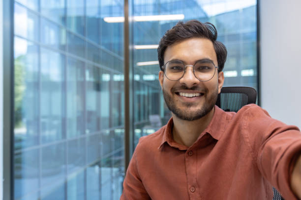 istock Smiling young businessman taking selfie in modern office with smartphone showing confidence and success 2174752299