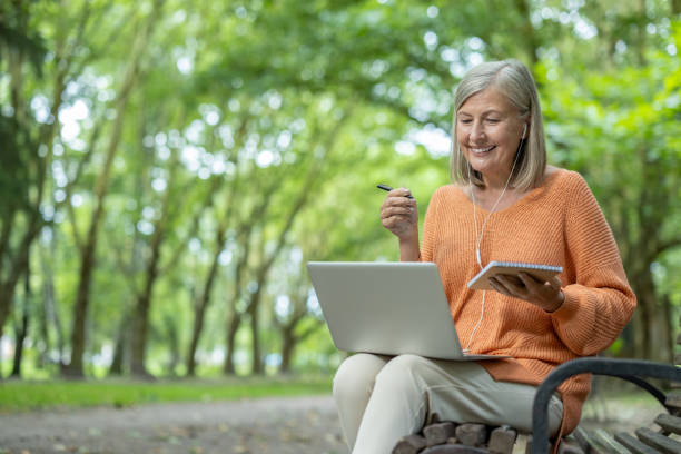 istock Mature woman enjoying online learning outdoors with a laptop and notebook in a peaceful natural setting 2174753077