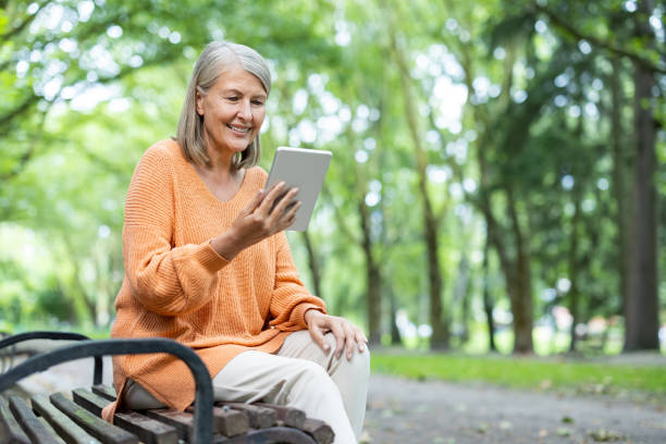 istock Smiling mature woman in orange sweater using tablet outdoors on park bench showcasing relaxed and connected lifestyle 2174753323