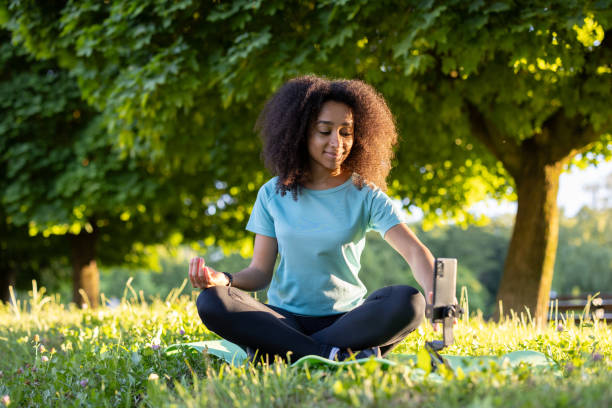 istock Young woman practices yoga outdoors in park, using smartphone for online class, surrounded by nature and sunlight 2174754944