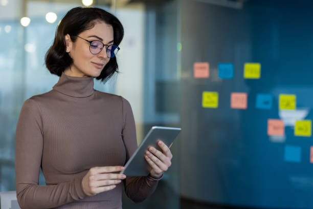 istock Confident businesswoman using tablet for planning and organization in modern office environment with sticky notes on glass wall 2174755168