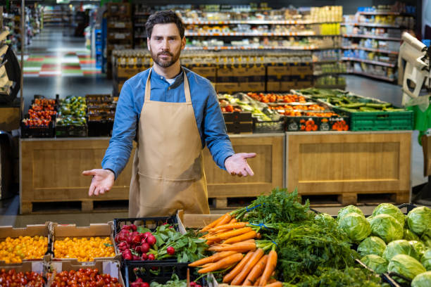 istock Friendly grocery store employee in apron presenting fresh vegetables at produce section of supermarket 2174755788