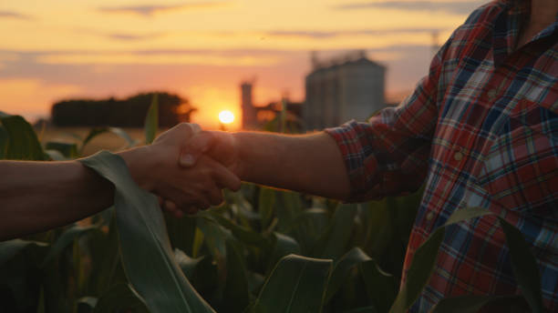 istock Caucasian Farmers Seal Agreement with Sunset Handshake by Corn Silo 2174756156