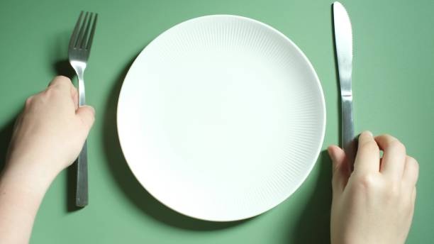 istock Female hands holding a fork and knife next to an empty plate on a green background close-up top view. 2174765932
