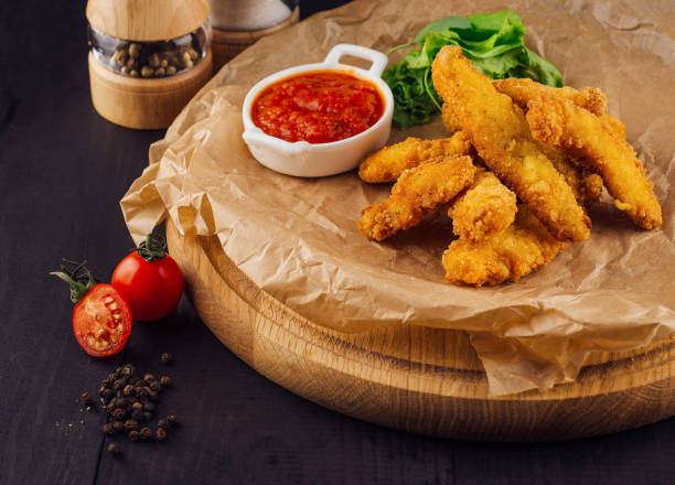 istock Breaded chicken strips lying on baking paper with spices around 2174771004
