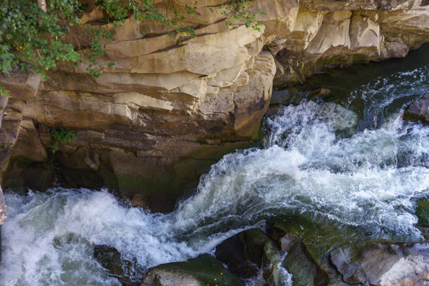 Closeup texture of rapid river with fresh cold water flowing through mountain rocks with foam and bubbles on sunny day. Nature force and power background.