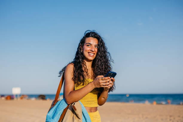 Young Woman Using Phone While Walking On The Beach In Barcelona In Spain