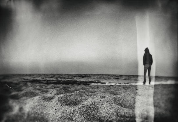 Heavy textured cretative image of lperson standing on empty beach looking out over the water.