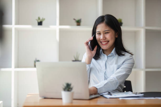 istock Professional Business Woman Talking on Phone While Working on Laptop in Modern Office Setting 2174839783