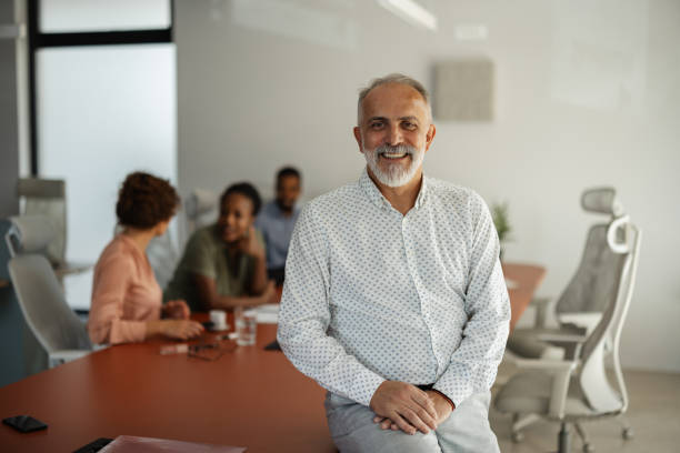 istock Mature man smiles while leaning on conference table. 2174843524