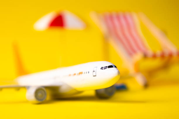 White miniature airplane in focus on a yellow background next to it has a hammock, umbrella with out of focus, concept of travel and flights