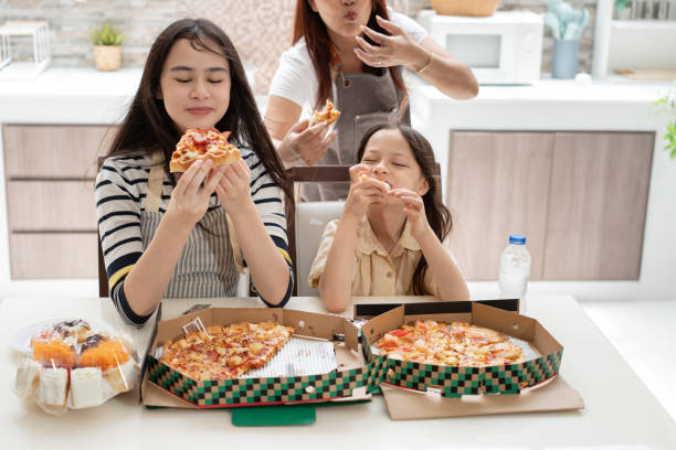istock Happy sibling with mother eating pizza in kitchen at home 2174866942